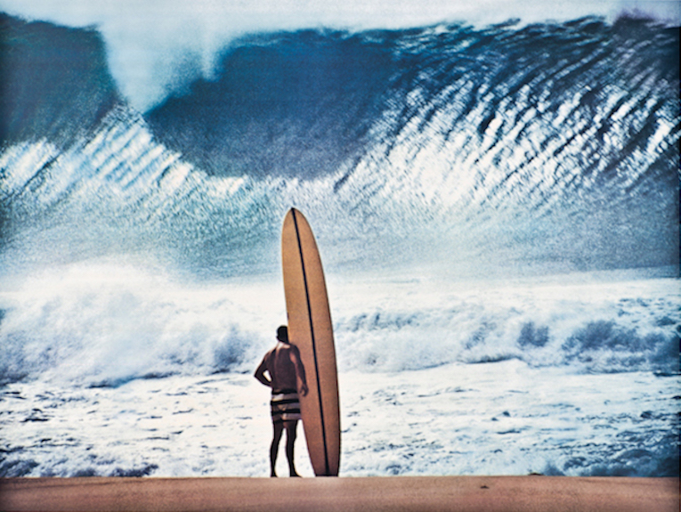 Greg Noll in his signature striped board shorts at Pipe, by John Severson